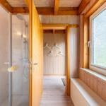 Dusche mit Glaswand, Holzverkleidung und Fenster mit Sitzbank.