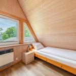 Ein Schlafzimmer mit Holzwand, Doppelbett, Nachttisch und Fenster mit Blick auf Grün.