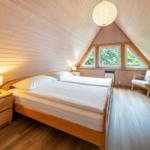 Schlafzimmer mit Doppelbett, Holzwand und Dreifachfenster mit Blick auf Grün.