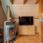 Wohnraum mit Kamin, Fernseher und Holzwand. Holzstuhl und Kaminholz sichtbar.