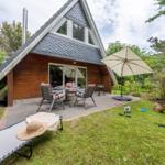 Haus mit Terrasse, Tisch, Stühlen, Sonnenschirm und Liegestuhl im Garten.