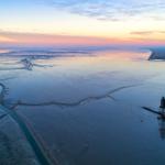 Aerial view of a lighthouse at sunset over a wide estuary with winding waterways.
