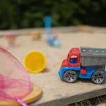 Ein Spielzeug-LKW steht auf Sand neben einem Netz und bunten Spielzeugen.