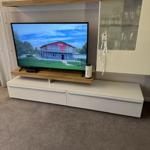 TV auf Holzregal, daneben Glaswand mit Gläsern und Dekoration.