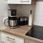 Küchenzeile mit Kaffeemaschine, Toaster und Herd. Holzoptik und weiße Schränke.