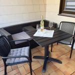 Terrasse mit Tisch, Stühlen und Sitzbank. Auf dem Tisch steht eine Weinflasche und zwei Gläser.