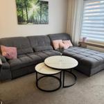 Ein Wohnzimmer mit grauem Sofa, zwei runden Tischen und einem Wandbild.