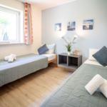 Zwei Betten mit Handtüchern, Wandbilder und Fenster mit Vorhängen.