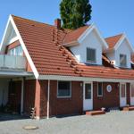 Rotes Dach, weiße Fassade, mehrere Fenster und eine Terrasse. Gravierter Boden vor dem Haus.
