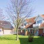 Haus mit rotem Dach, grünem Garten und Spielplatz. Balkon und Sonnenschirm sichtbar.