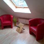 Zwei rote Sessel und ein Glas-Tisch unter einem Dachfenster mit Holzboden.