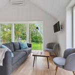 Ein Wohnzimmer mit grauem Sofa, zwei Stühlen und großen Fenstern zum Garten.