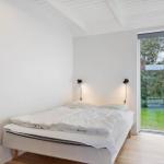 Schlafzimmer mit Bett, zwei Wandlampen und Glasschiebetür zum Garten.