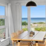 Esszimmer mit Tisch, Stühlen und Meerblick durch große Fenster.