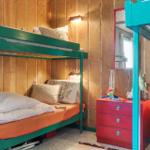 Zimmer mit zwei Etagenbetten, rotem Schrank und Holzwandverkleidung.