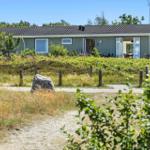 Ein graues Haus mit offenen Türen und Fenstern. Gras und Bäume umgeben es.