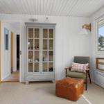 Raum mit grauem Schrank, Sessel und Fenster. Küchenbereich links sichtbar.