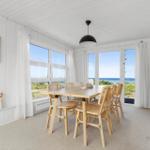 Esszimmer mit Tisch, Stühlen und Meerblick durch große Fenster.