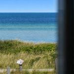 Meeransicht durch Fenster mit Gras und Holzpfosten im Vordergrund.