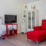 Ein Wohnzimmer mit rotem Sofa, weißer Wand und TV auf rotem Möbel.