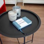 Runde Tisch mit Buch und zwei Kerzen auf Holzboden.