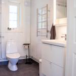 Badezimmer mit Toilette, Waschbecken und Dusche. Fenster, Handtuchhalter und Spiegel sichtbar.