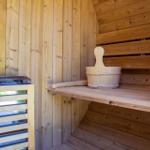 Holzsauna mit Sitzbank, Eimer und Ofen. Außenansicht durch Fenster sichtbar.