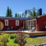 Rotes Holzhaus mit Terrasse, Sauna und Garten. Grill und Sitzmöbel auf der Veranda.