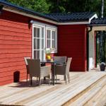 Roter Holzhaus mit Terrasse, Tisch und Stühlen, umgeben von Bäumen.