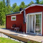 Rotes Holzhaus mit Terrasse, Sitzgelegenheit und Gartentisch. Hintergrund: Wald.