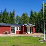 Rotes Holzhaus mit Terrasse, Garten und Flagge vor Wald.