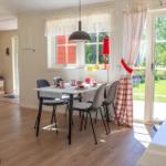 Esszimmer mit Tisch, Stühlen und Blick auf Garten. Rote Gardinen und Lampe.