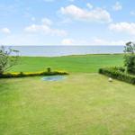 Großer Garten mit Trampolin und Meerblick. Grünfläche, Bäume und Himmel.