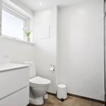 Badezimmer mit Toilette, Waschbecken und Dusche. Fenster mit Blumen auf dem Sims.
