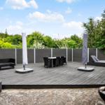 Terrasse mit Sitzgruppe, Esstisch und Liegen. Umgeben von Grün und Zaun.