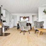 Wohnzimmer mit Holzboden, Kamin und Sesseln. Essbereich und Küche im Hintergrund.