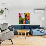 Ein Wohnzimmer mit blauem Sofa, grauer Sessel und Holztisch. An der Wand hängt ein abstraktes Gemälde.