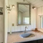 Badezimmer mit Waschbecken, Spiegel und Fenster. Wandverkleidung und Dachbalken sichtbar.