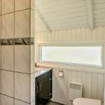 Badezimmer mit Fliesenwand, Waschbecken und Toilette unter einem schrägen Dach