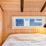 Schlafzimmer mit Holzwandverkleidung, Bett und Fenster. An der Wand hängen zwei Bilder.
