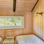 Zimmer mit Holzwand, Bett, Stuhl und Fenster zur grünen Landschaft.