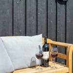 Holzbank mit Kissen, Weinflasche und zwei Gläser auf einer Terrasse.