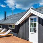 Schwarzes Holzhaus mit Terrasse und Liegestühlen unter blauem Himmel.