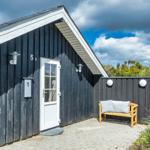 Schwarze Holzhütte mit weißer Tür und Bänke auf gepflastertem Hof