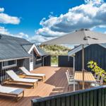 Terrasse mit Liegestühlen, Tisch und Sonnenschirm vor einem Haus mit Holzverkleidung.