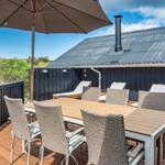 Terrasse mit Tisch, Stühlen und Sonnenschirm. Hintergrund: Haus mit dunklem Holz und Wellblechdach.