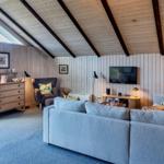 Wohnzimmer mit Sofa, Fernseher und Holzwandverkleidung unter schrägen Dachbalken.