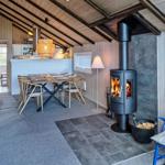 Wohnraum mit Kaminofen, Esstisch und Sofa. Holzdecke und Wandverkleidung.