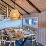 Essbereich mit Holztisch, Stühlen und Lampe. Küche im Hintergrund. Holzwände und Dachbalken.