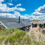 Holzhaus mit Dachterrasse und Sonnenschirm zwischen Gras und Himmel.